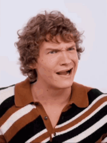 a man with curly hair wearing a striped shirt making a funny face