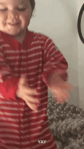 A baby in striped pajamas dances and claps beside a pile of toys.