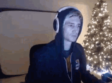 a man in a hoodie and headphones is sitting in front of a christmas tree .