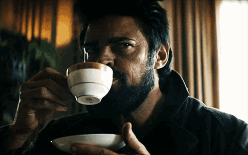 a man with a beard is drinking from a small white cup