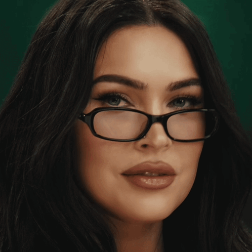 A woman with dark hair and glasses gives a sultry look.