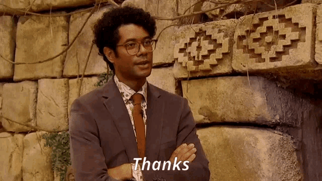 a man in a suit and tie stands in front of a stone wall and says thanks