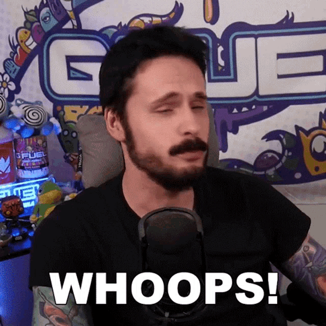 a man with a beard is sitting in front of a microphone and says " whoops "