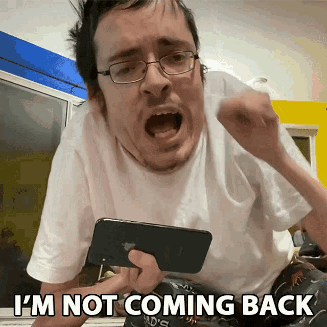 a man with glasses is holding a cell phone and screaming that he 's not coming back