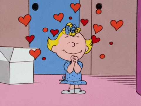 Linus smiles with clasped hands as red hearts float around him.