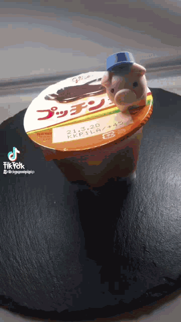 a stuffed pig is sitting on top of a container of pudding