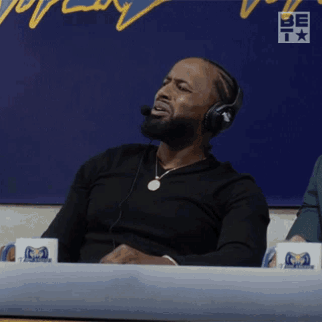 a man wearing headphones and a necklace sits at a table with two cups that say rams on them