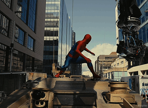 a man in a spiderman costume stands on top of a vehicle in a city street