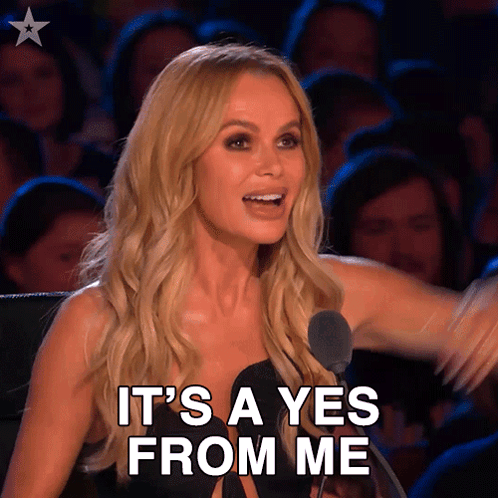 Amanda Holden smiles at a judging desk with “IT’S A YES FROM ME.”