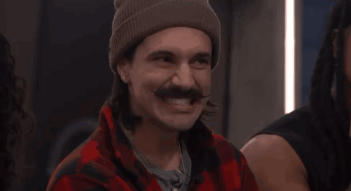 a man with a mustache wearing a beanie and a plaid shirt smiles