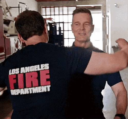 two men wearing los angeles fire department shirts are hugging each other