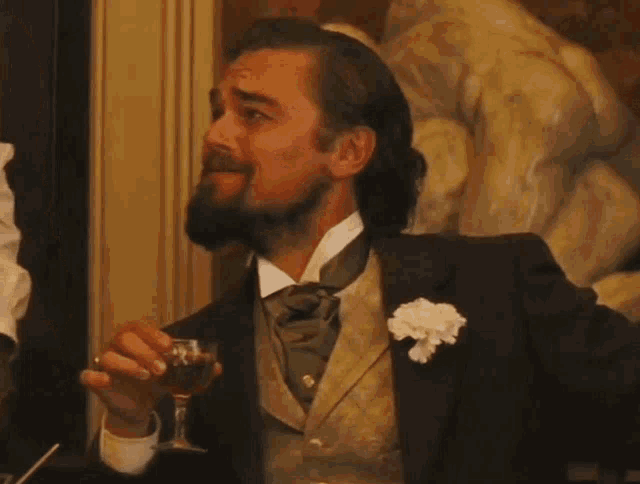 Leonardo DiCaprio laughs while holding a drink in a lavish room.