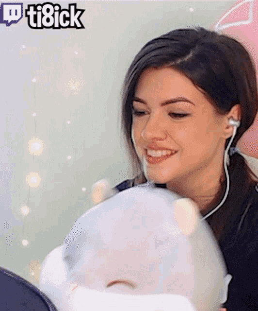 a woman is smiling while holding a stuffed animal with a twitch logo in the background