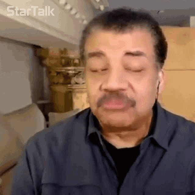 a man with a mustache is wearing ear buds and making a funny face with his eyes closed .