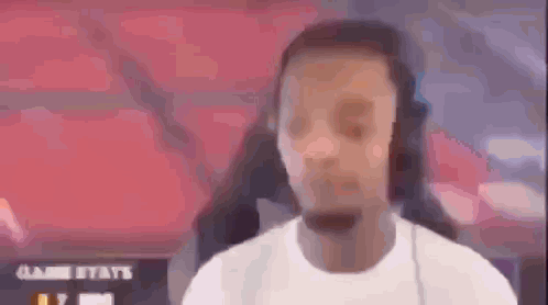 a man wearing headphones and a white shirt is standing in front of a red wall .