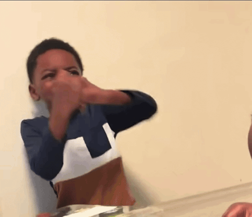 a young boy in a blue and white shirt is laughing with his mouth open