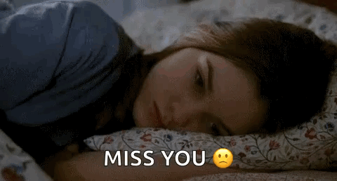 A woman lies on a bed looking sad beneath “MISS YOU.”