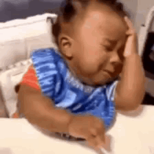 A baby rubs its eye while crying in a high chair.