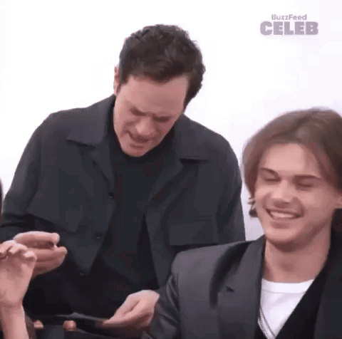 two men are sitting at a table with their eyes closed and one of them is holding a cell phone .