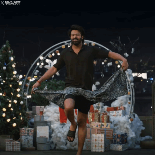a man in a black shirt is dancing in front of a christmas tree and gifts