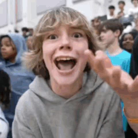 a young boy is making a funny face with his mouth open in front of a crowd of people .