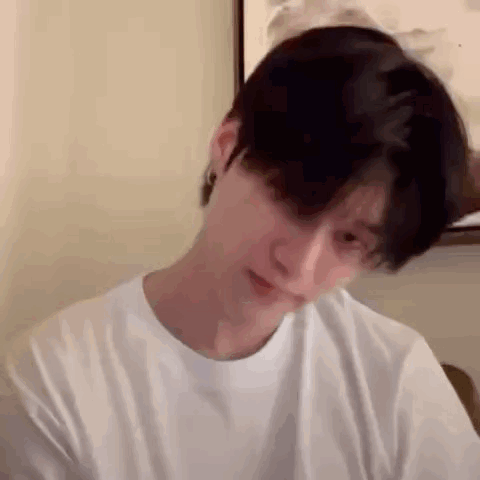 a young man with black hair is wearing a white t-shirt and earrings .