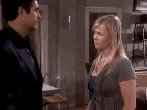 a man and a woman are standing next to each other in a living room and looking at each other .