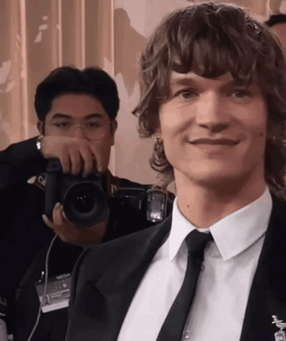 Connor Storrie smiles subtly while another person films behind him.