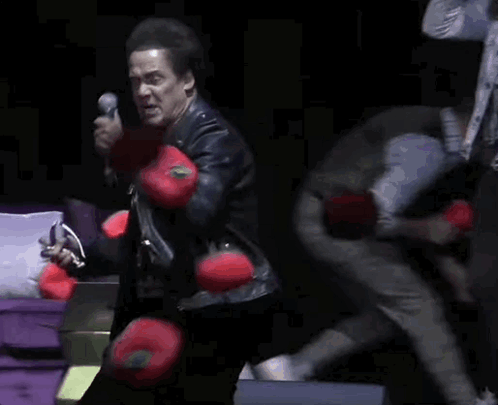a man singing into a microphone with a woman behind him holding boxing gloves