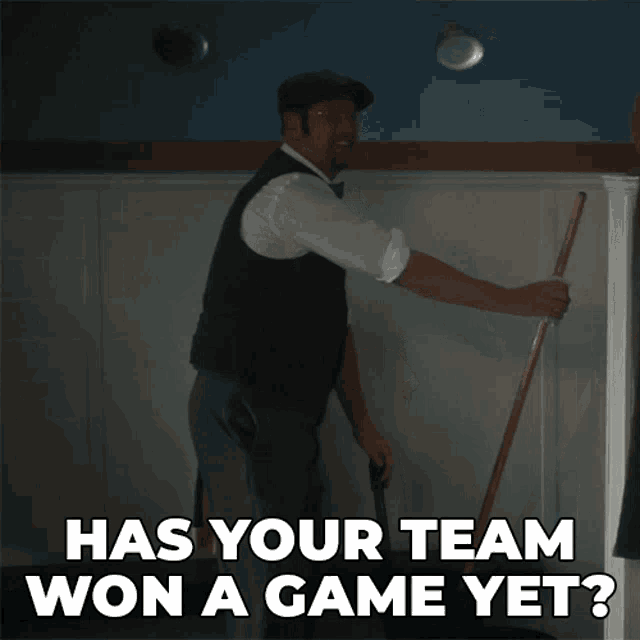 a man is holding a mop in front of a wall and says has your team won a game yet