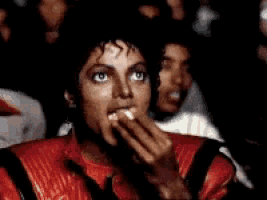 Michael Jackson eats popcorn while watching intently in a crowd.