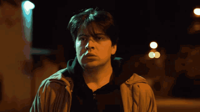 a man in a brown jacket is standing in front of a street light at night