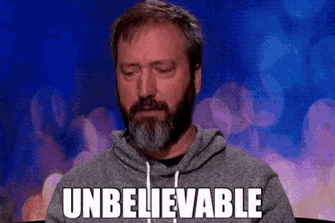 a man with a beard is sitting in front of a microphone with the words `` unbelievable '' on his face .