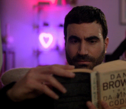 a man with a beard is reading a book called dan brown 's damn code
