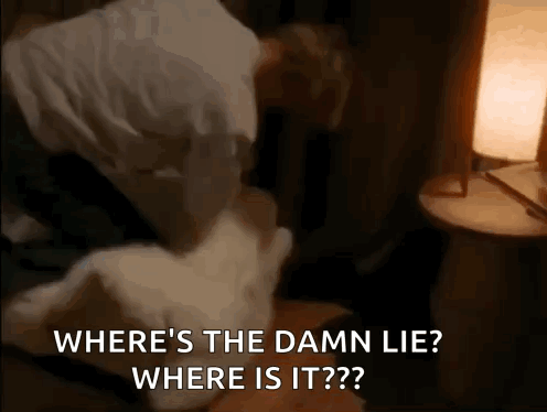 a man is laying on a bed with a pillow and a lamp and says where 's the damn lie ?