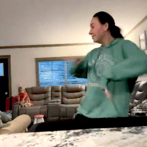 a woman in a green hoodie is dancing in front of a living room