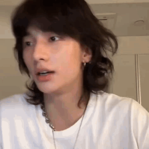 a close up of a person 's face with long hair wearing a white shirt and a necklace .