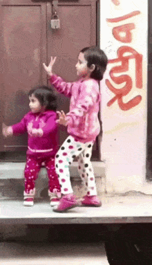 A small child in bright pink pajamas dances outside a doorway.