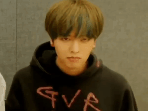 a young man in a black hoodie is holding a bottle in his hand and looking at the camera .