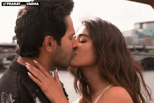 A couple kisses outdoors while the woman holds the man's neck.