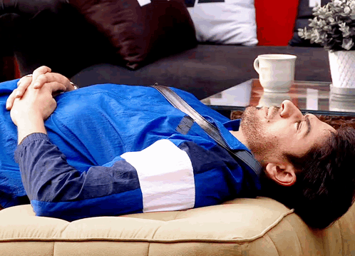 a man in a blue jacket is laying down on a couch