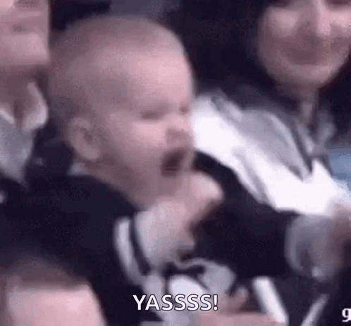 A baby cheers excitedly while being held among a crowd.