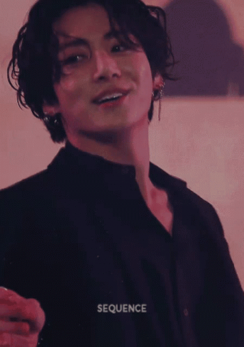 A performer in dark clothing looks toward the camera under red stage light.