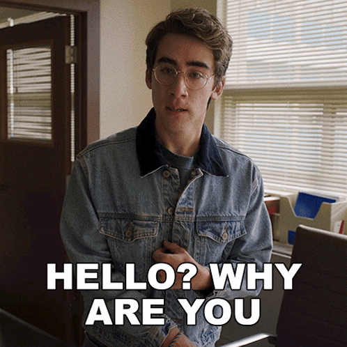 a young man in a denim jacket is standing in front of a window and says hello why are you