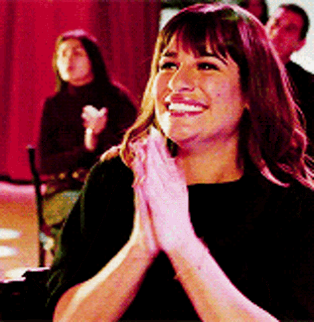 Rachel Berry from Glee smiles and claps in an audience.