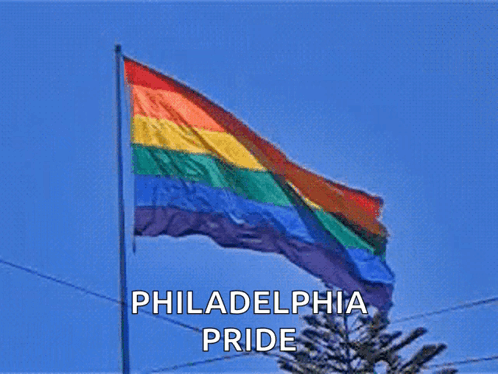 a philadelphia pride flag is flying in the wind against a blue sky