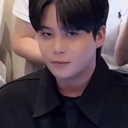 a young man wearing a black shirt and tie is looking at the camera .