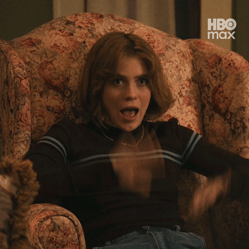 A woman sitting in an armchair opens her mouth in exaggerated surprise.