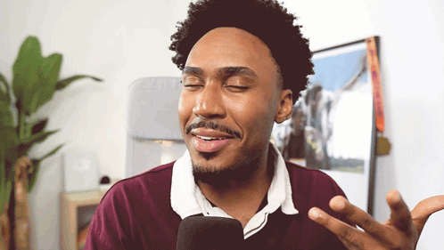 a man in a maroon shirt is talking into a microphone and smiling
