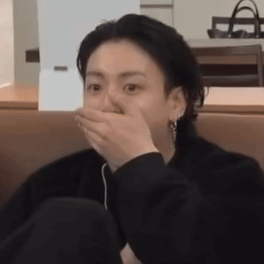 A seated person covers their mouth with one hand in disbelief.